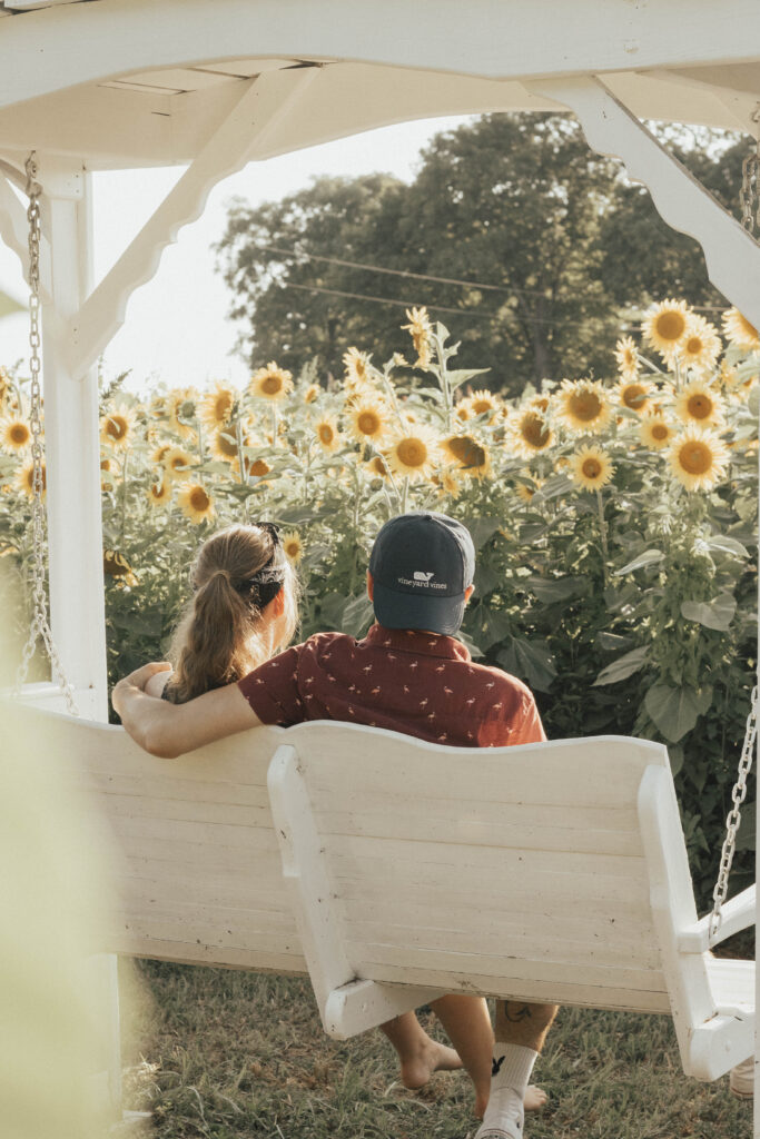A couple sitting on a porch swing overlooking a sunflower field