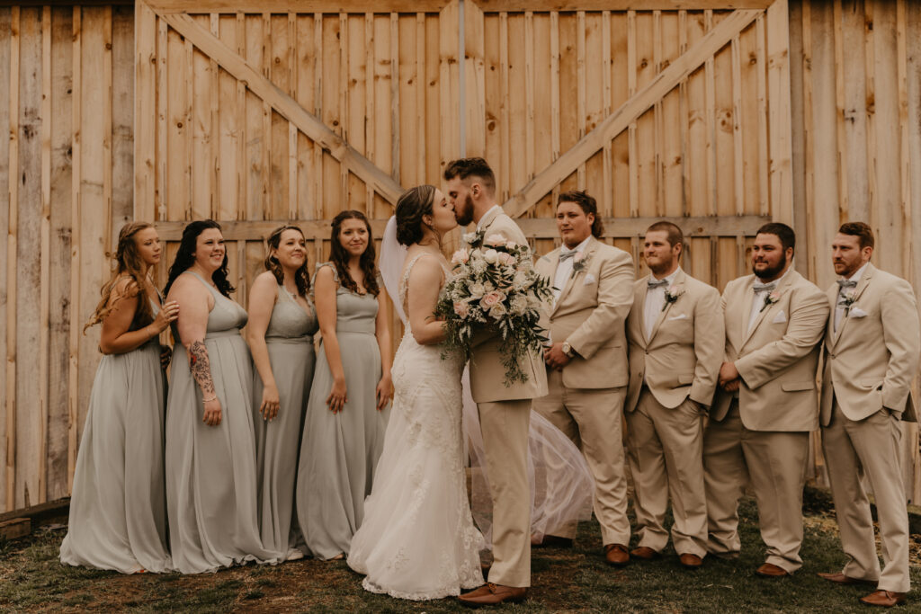 A wedding party and kissing couple in front of their barn wedding venue at 22 Acres Farm in Ohio