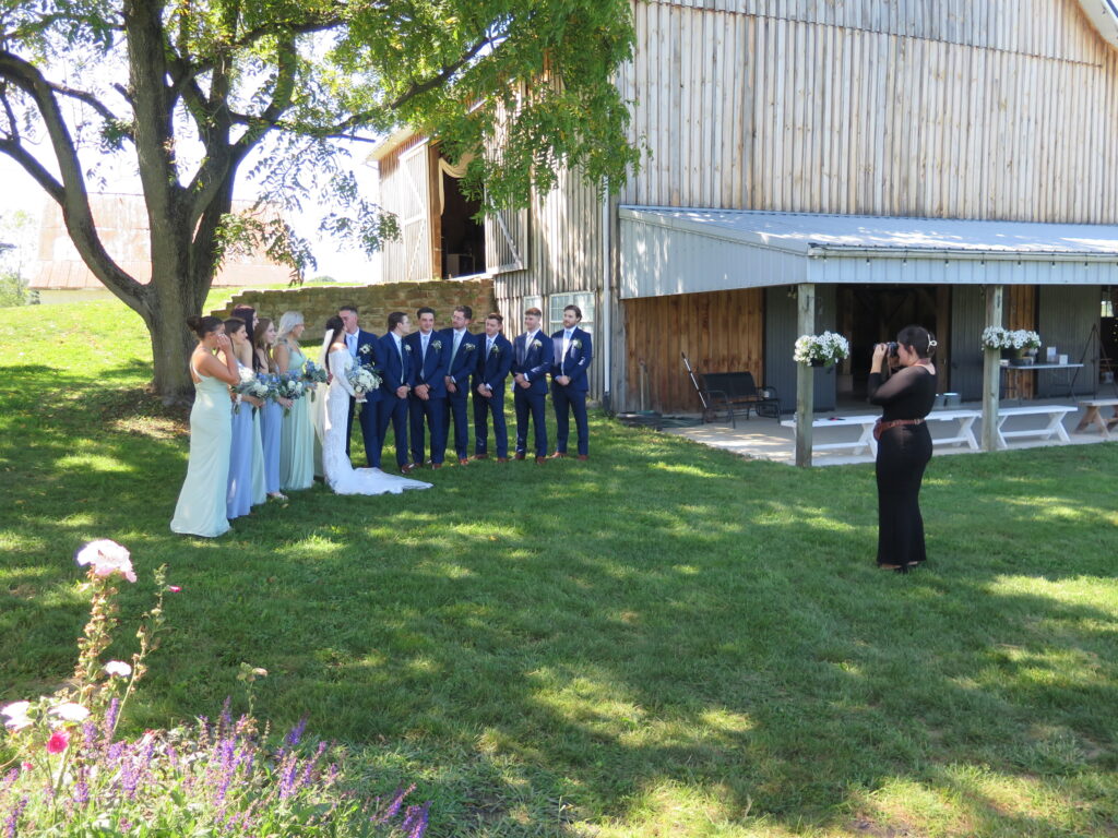 Photographer capturing a joyful bridal party posing for wedding photos at a scenic Columbus, Ohio venue, with the bride and bridesmaids smiling in their elegant dresses.