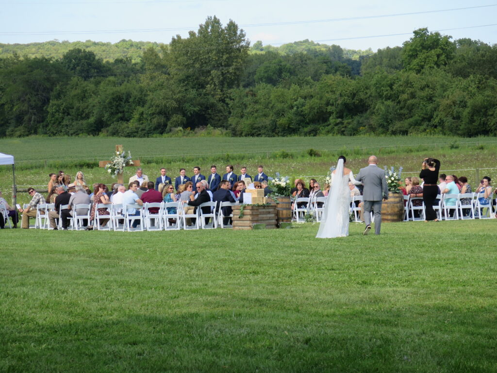 Bride walking down the aisle during her wedding ceremony at a stunning outdoor venue in Columbus, Ohio, with guests watching and a scenic backdrop.