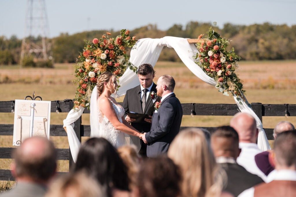 A joyful bride and groom holding hands under a rustic wooden arch adorned with flowers at 22 Acres Farm, a Columbus Ohio venue.