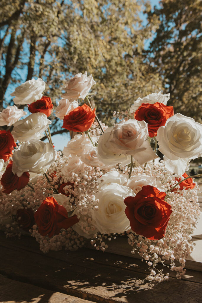 A bouquet of red and white roses with airy baby's breath sits on a wooden table at 22 Acres Farm near Columbus, Ohio. Sunlight filters through the trees, highlighting the romantic floral details.