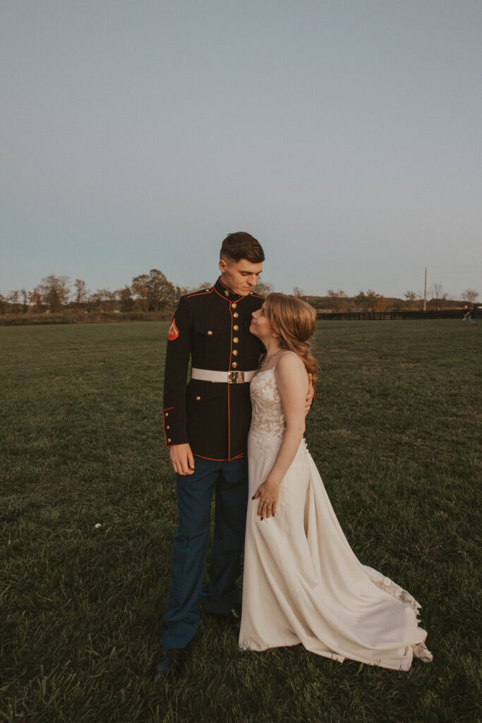 A Marine groom and his bride share a tender embrace in an open field at 22 Acres Farm near Columbus, Ohio. The fading sunlight enhances the romantic countryside setting.