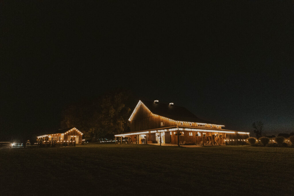 The barn at 22 Acres Farm near Columbus, Ohio, glows with string lights against the night sky. The warmly lit venue creates a cozy and romantic atmosphere for the wedding celebration.