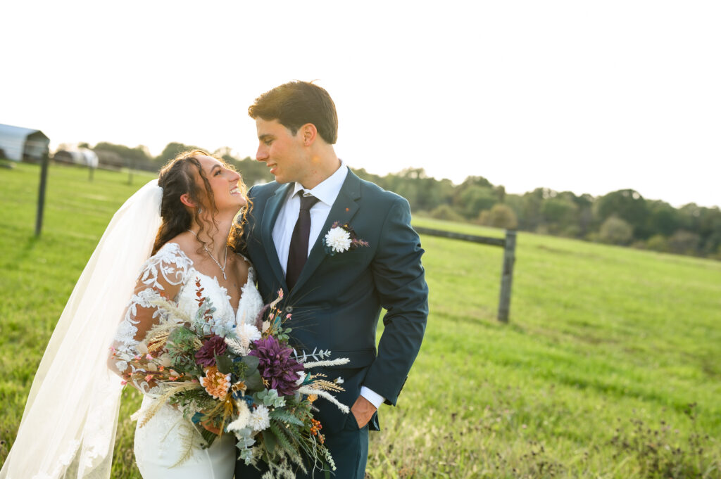 The newlyweds pose in golden evening light with open pastures behind them at 22 Acres Farm. The bride’s wildflower bouquet and the groom’s dark green suit complement the earthy tones of their outdoor Ohio wedding.