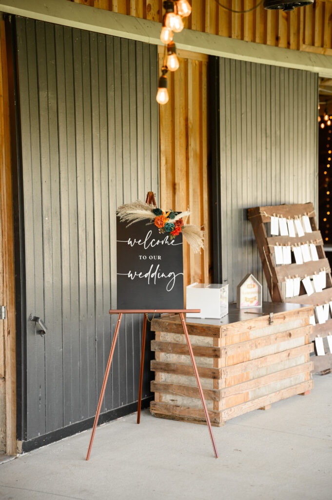 A chalkboard-style welcome sign greets guests outside the barn at 22 Acres Farm. Accented with pampas grass and terracotta-toned florals, it reflects the couple’s earthy wedding aesthetic and handcrafted details.